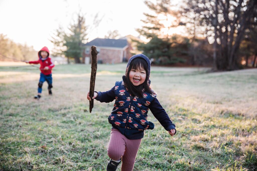 Two children running in a field with a stick, capturing the light within.