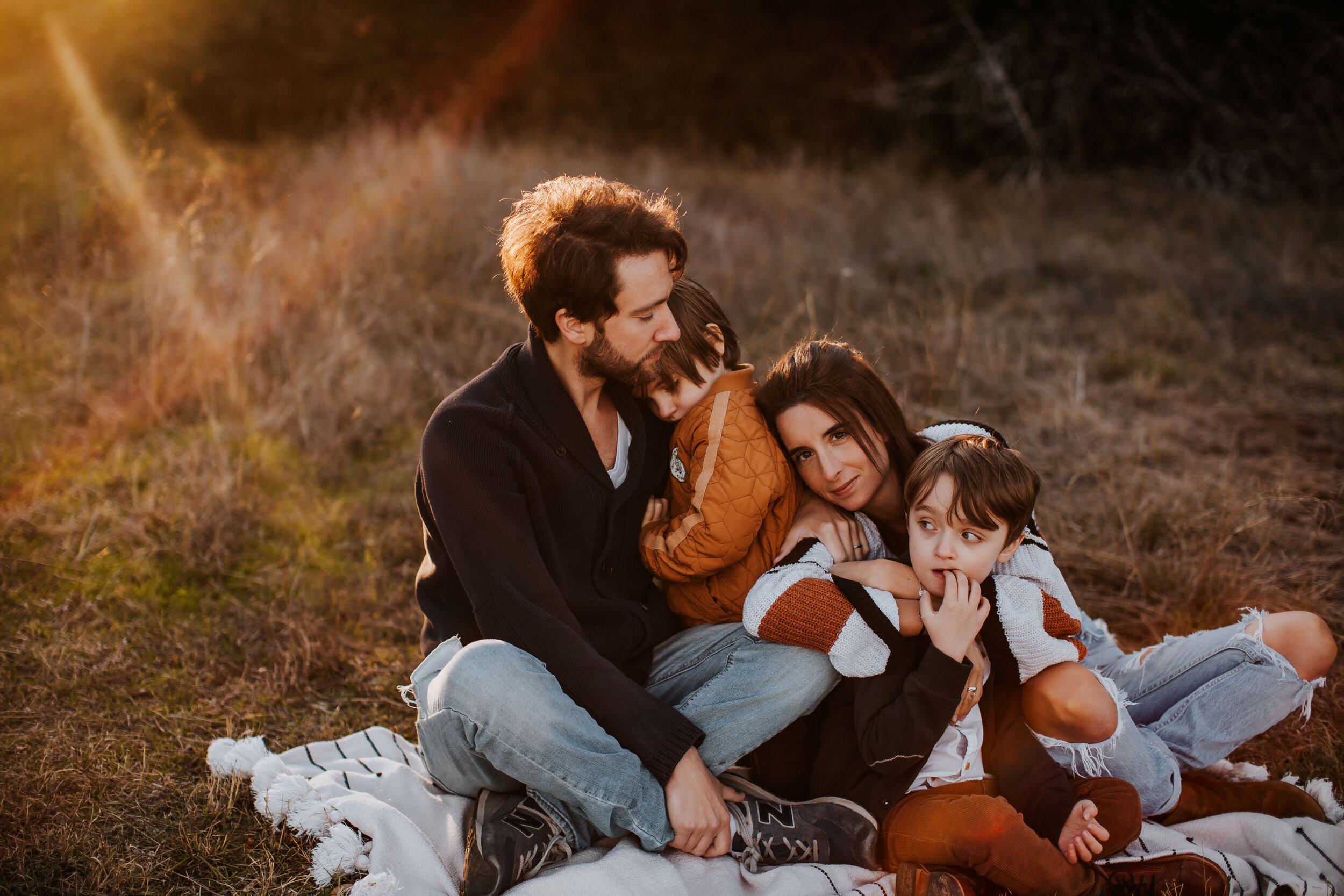 A family sits on a blanket in a field at sunset.