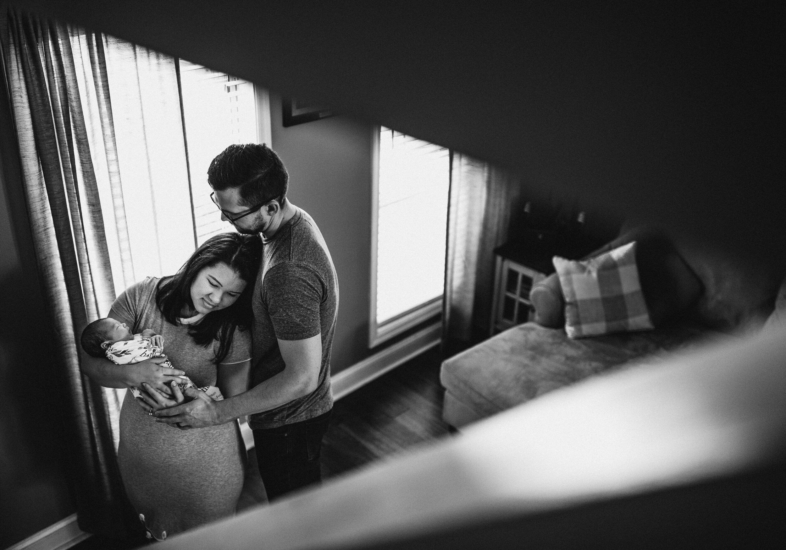 Black and white photo of a couple holding a baby in the living room.