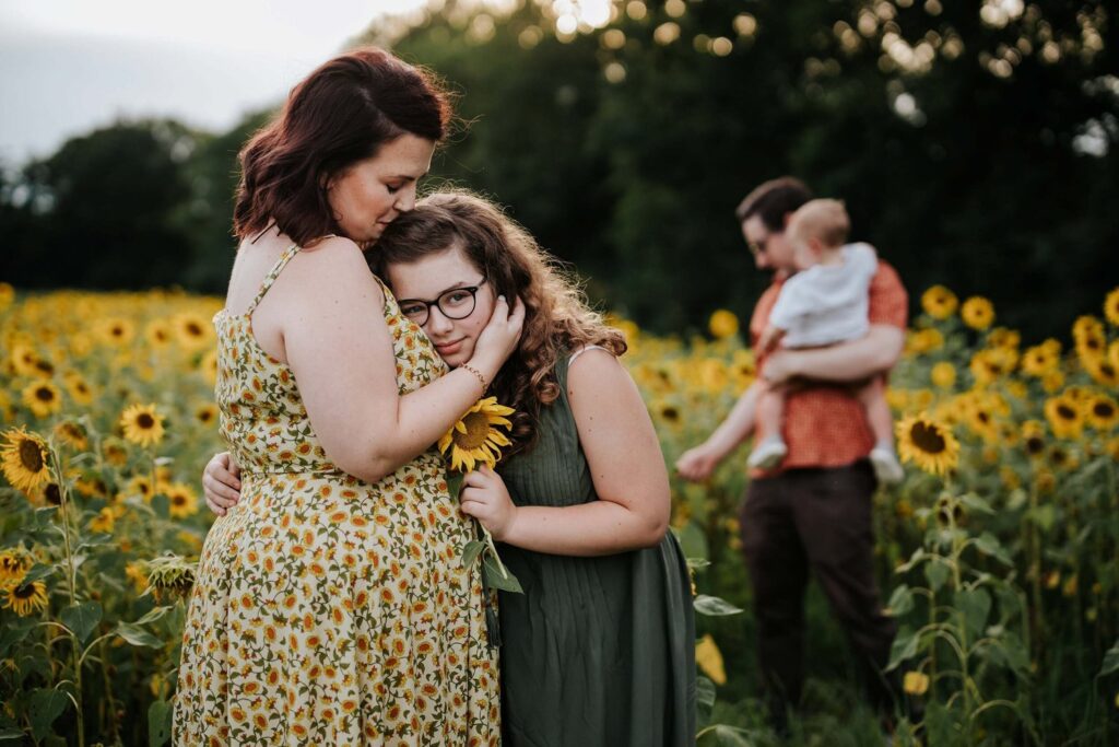 A mother and daughter embracing in a field of sunflowers.