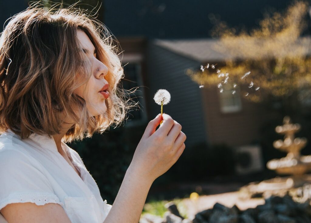 A young woman blowing a dandelion in a personal moment.