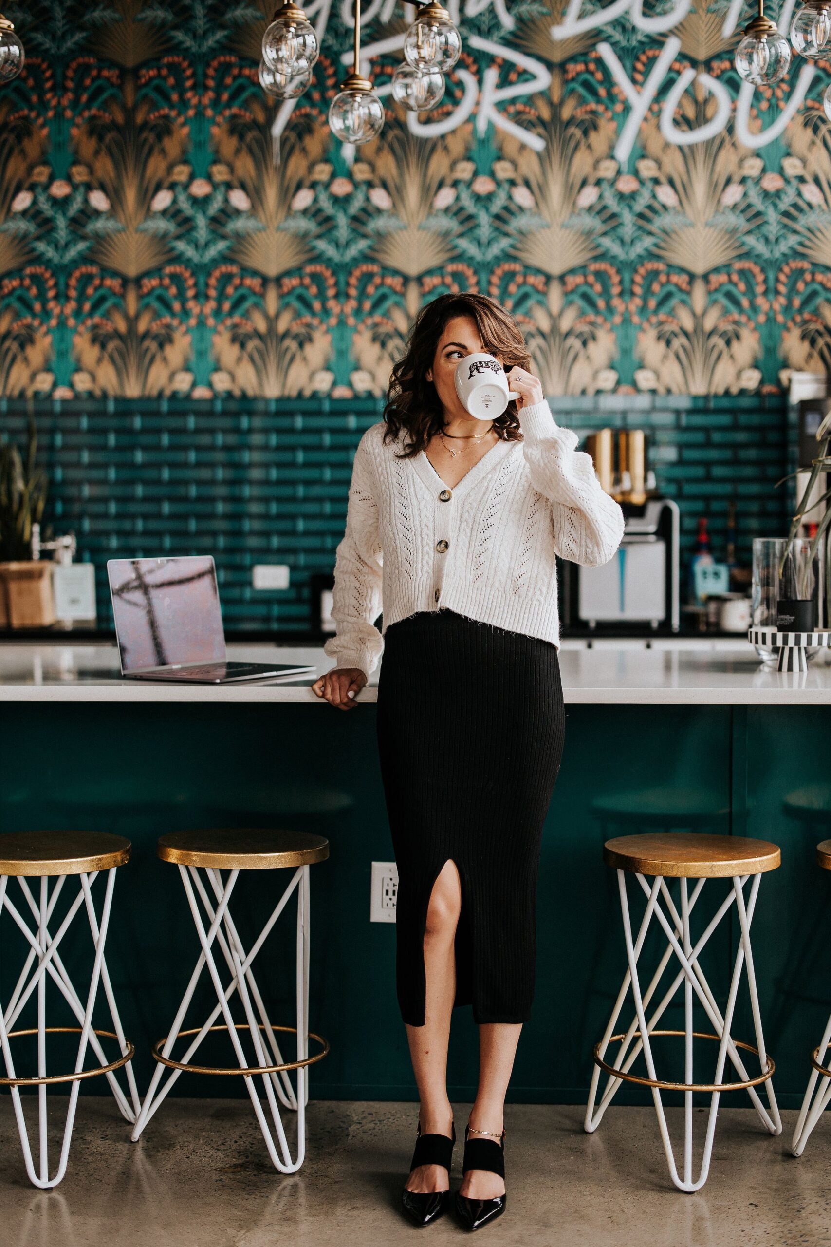 A person standing at the counter of a coffee shop holding a cup of coffee.