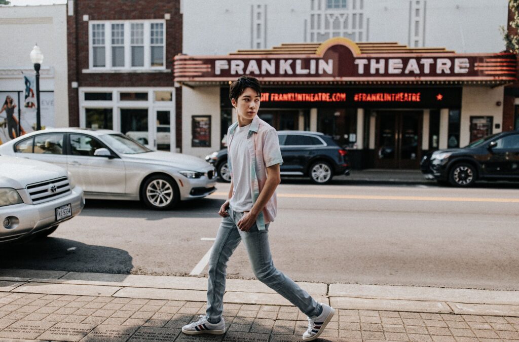 A personal young man walking down the street in front of a theater.