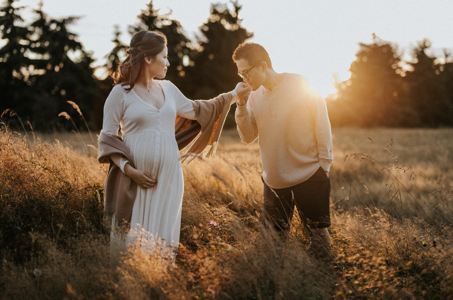 A pregnant couple in a field at sunset, capturing a beautiful moment in one of Portland Oregon's scenic family photo locations.